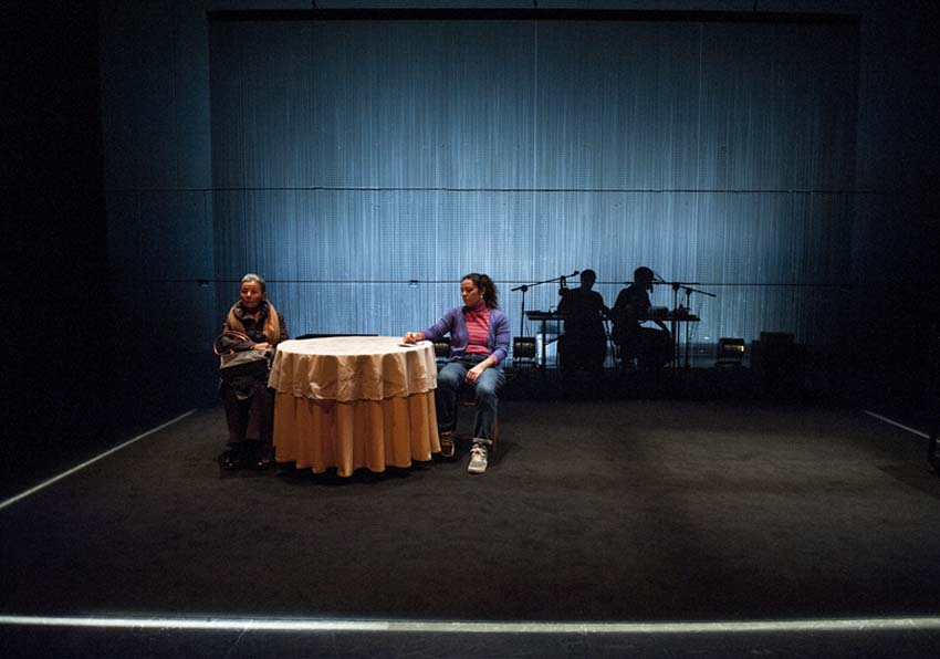 Two actresses in front of a table and two musicians in the background